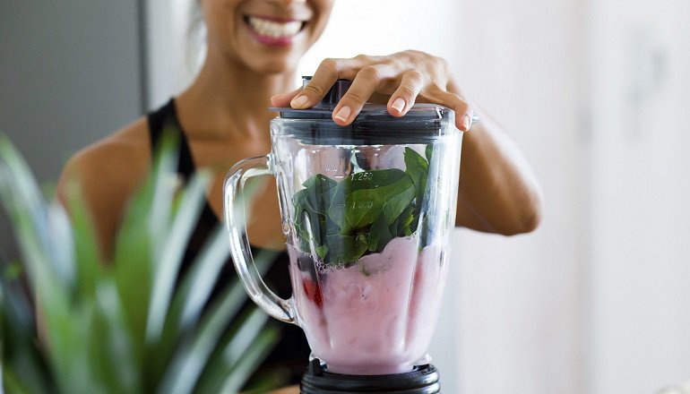 Woman blending spinach, berries, bananas and almond milk to make a healthy green smoothie